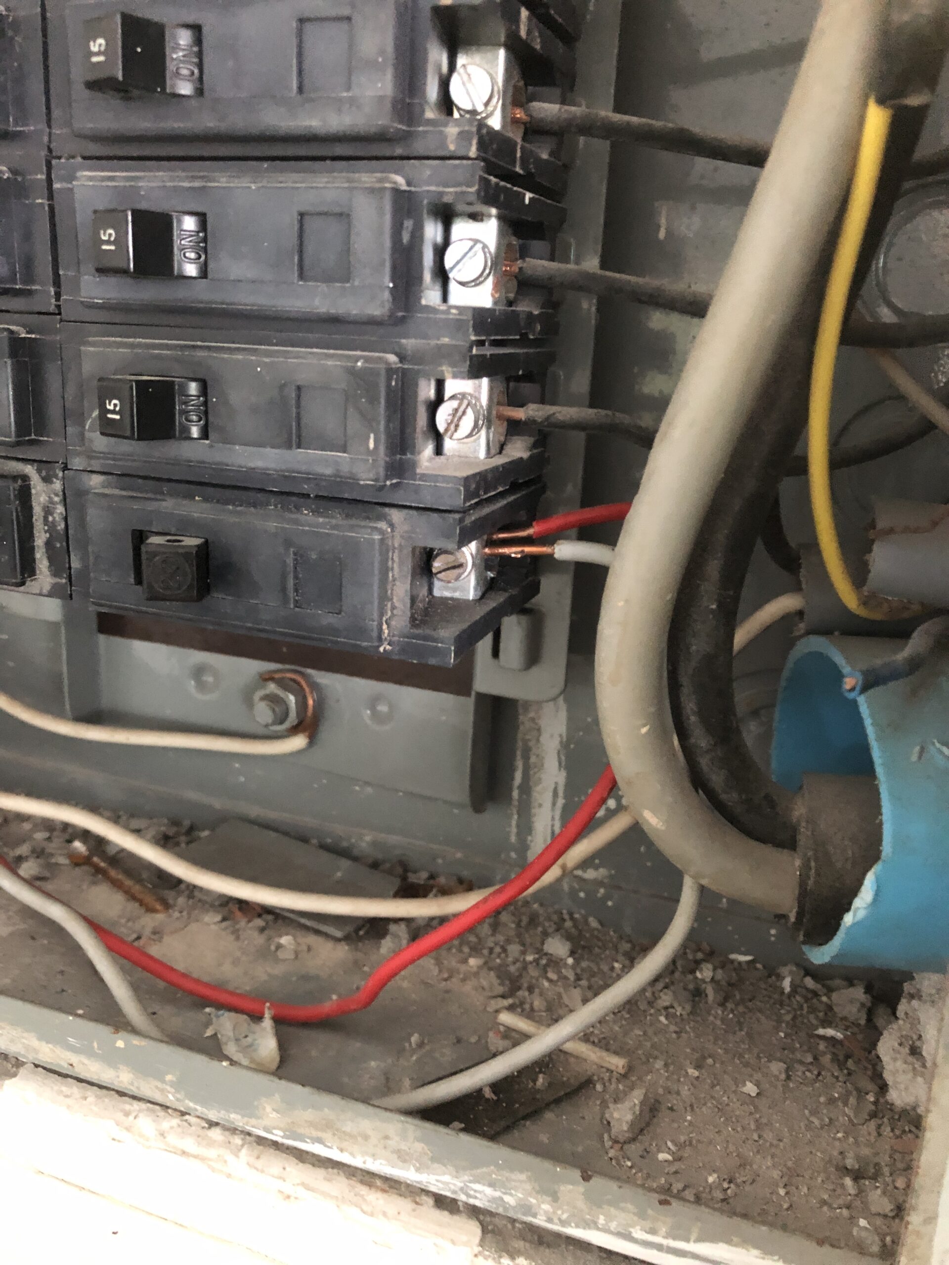 Dangerous double-tapped circuit breaker terminal with exposed wires inside a dusty electrical panel.