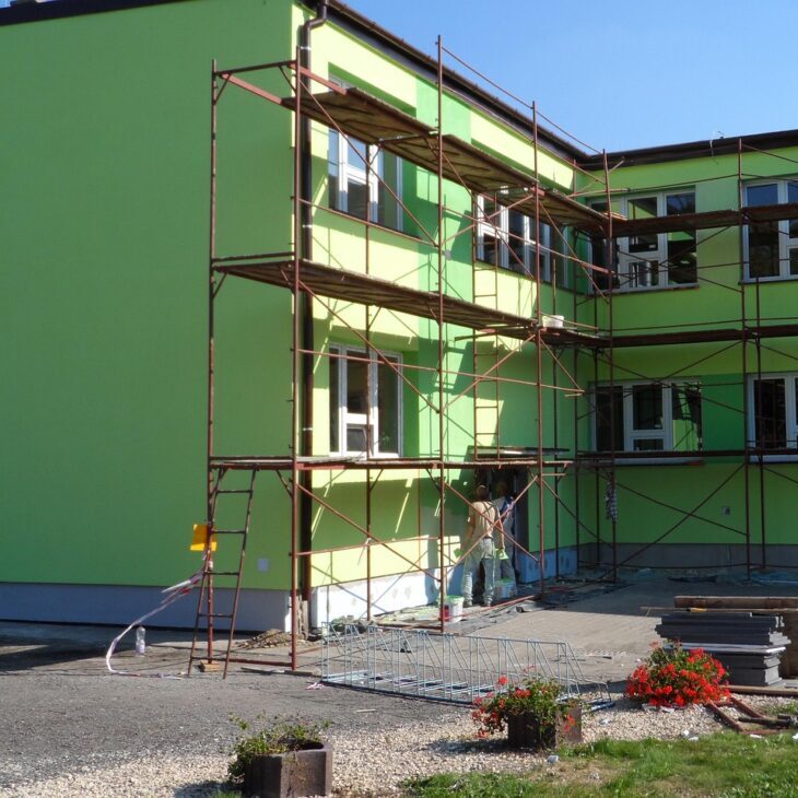 Multi-tier steel scaffolding erected against a bright green commercial building during an exterior renovation and painting project in Pattaya.