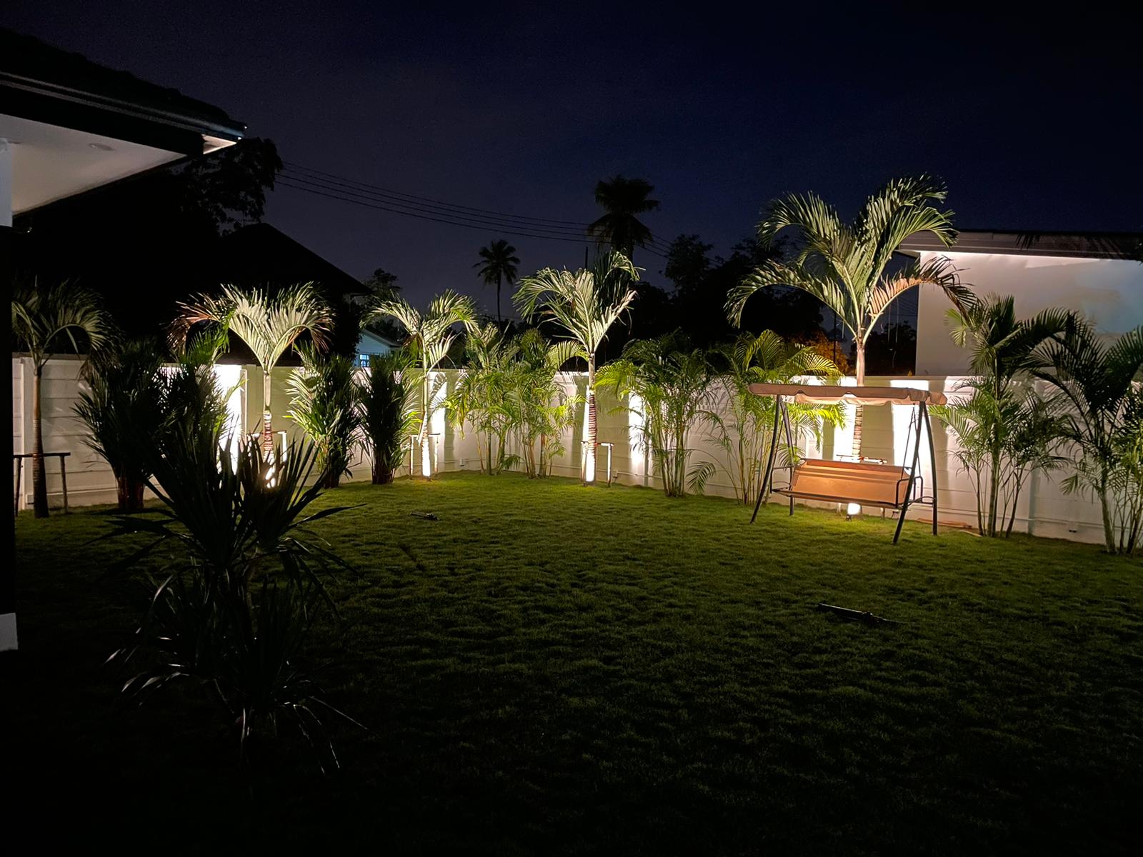 Nighttime view of a residential garden with custom landscape lighting and colorful accent tree uplighting in Pattaya