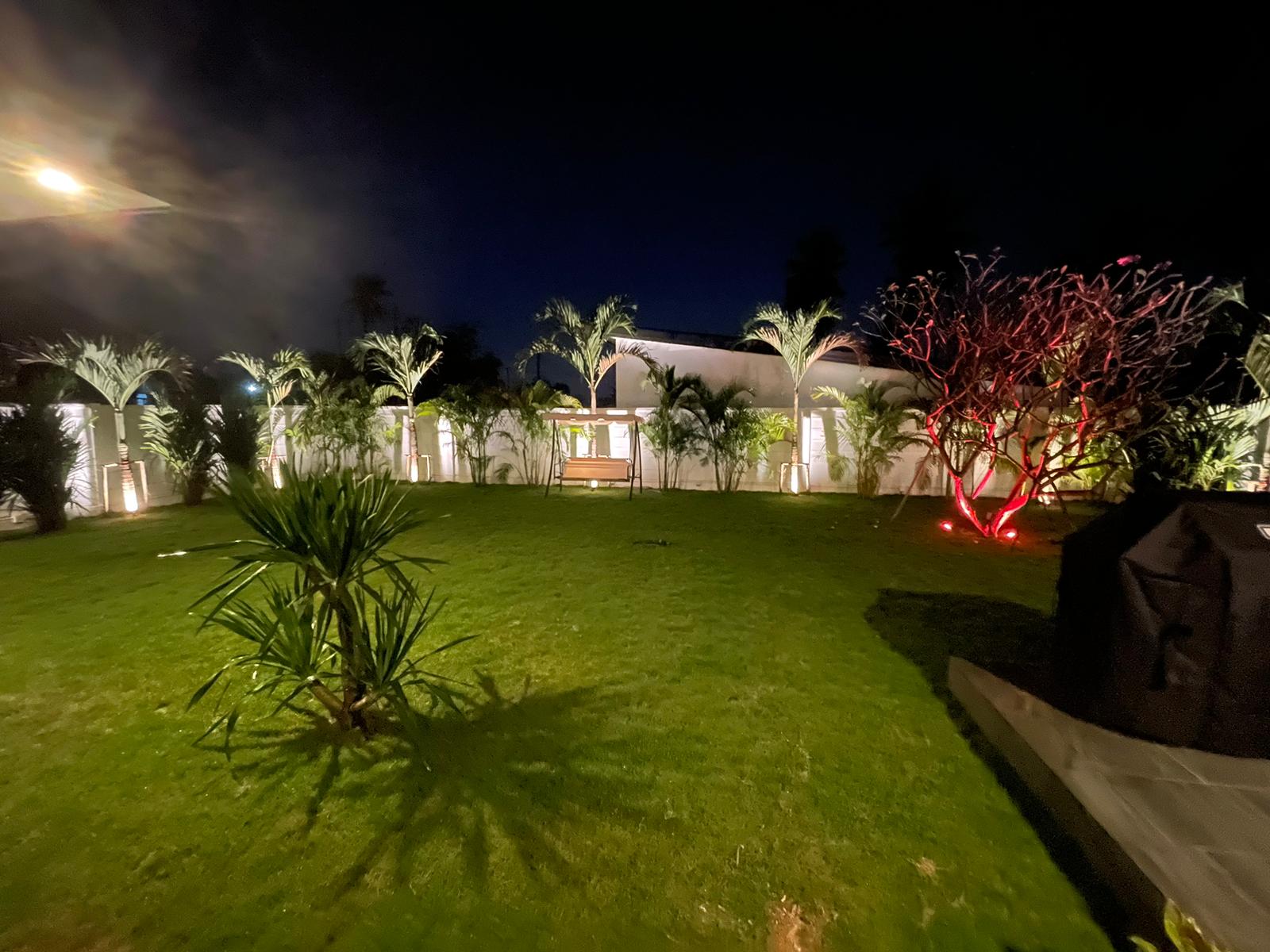Nighttime view of a residential garden with custom landscape lighting and colorful accent tree uplighting in Pattaya