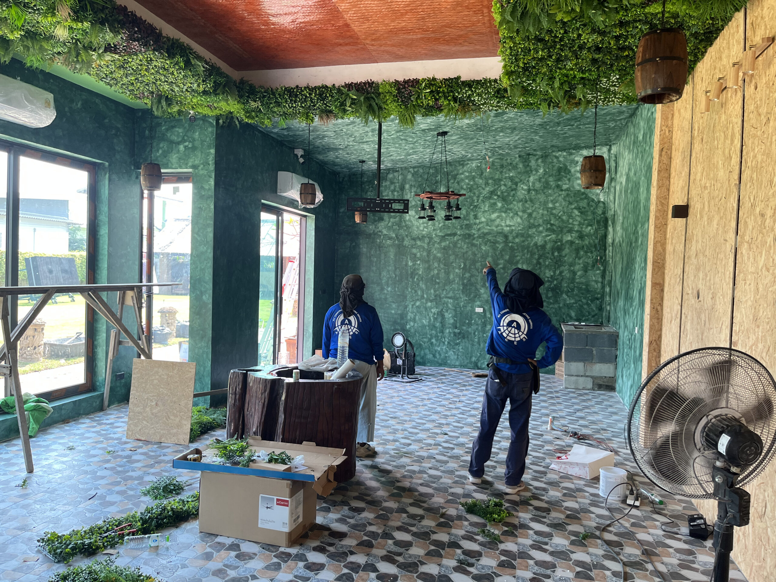 Workers inside a commercial interior fit-out featuring green textured walls, ceiling foliage, and decorative lighting