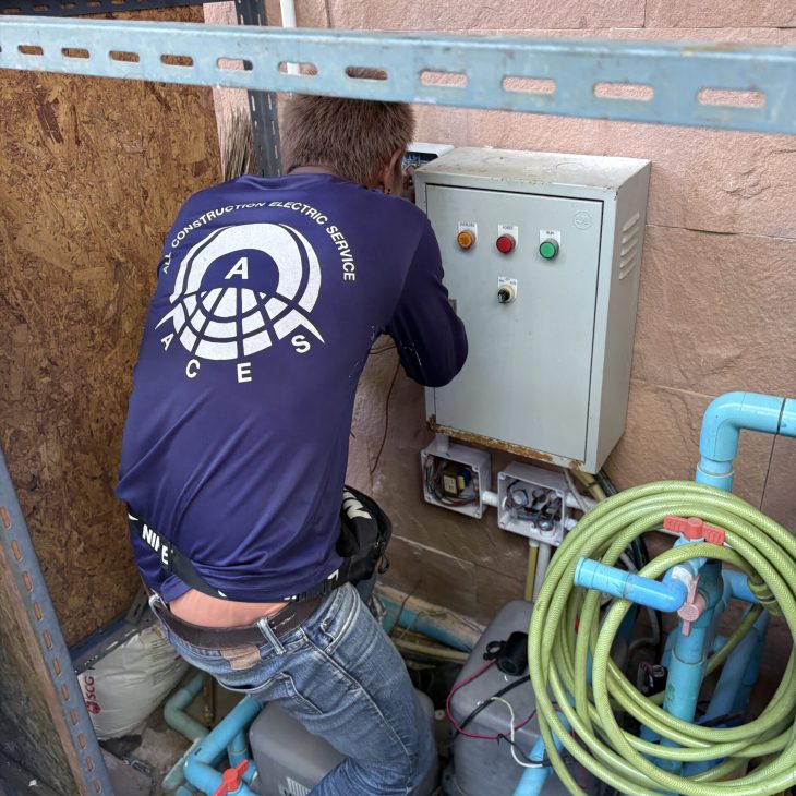 An ACES Pattaya technician wearing a branded company uniform while working on an outdoor electrical automation control panel.
