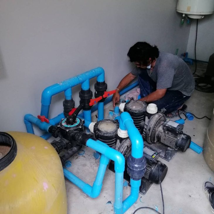 A professional technician installing and configuring a complex dual-pump swimming pool filtration and plumbing system in Pattaya.
